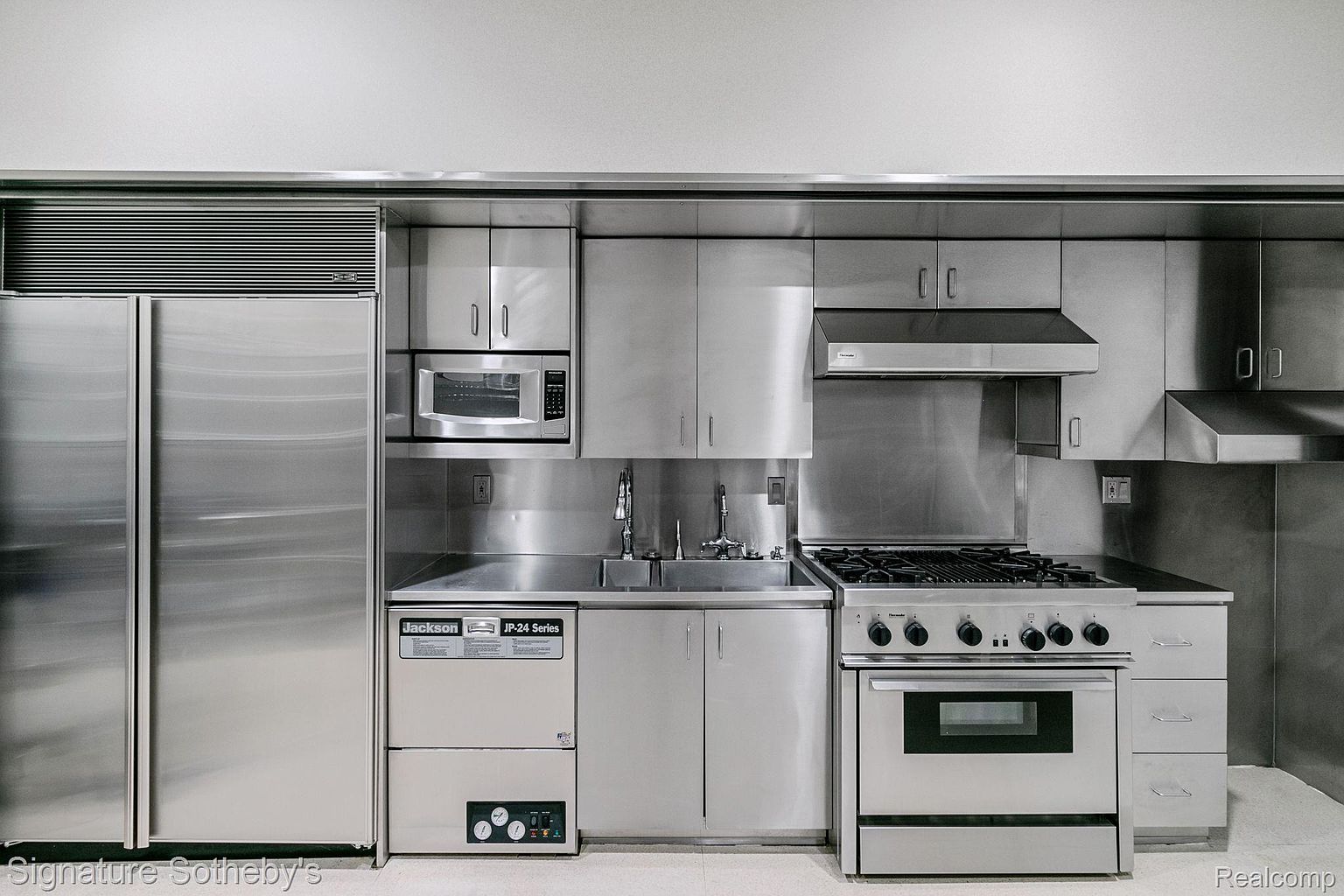 This is a commercial-style kitchen featuring stainless steel appliances and cabinetry. The kitchen includes a large refrigerator, microwave, dishwasher, sink, and a professional-grade stove with an oven. The overall impression is clean, functional, and modern, suitable for high-volume cooking.