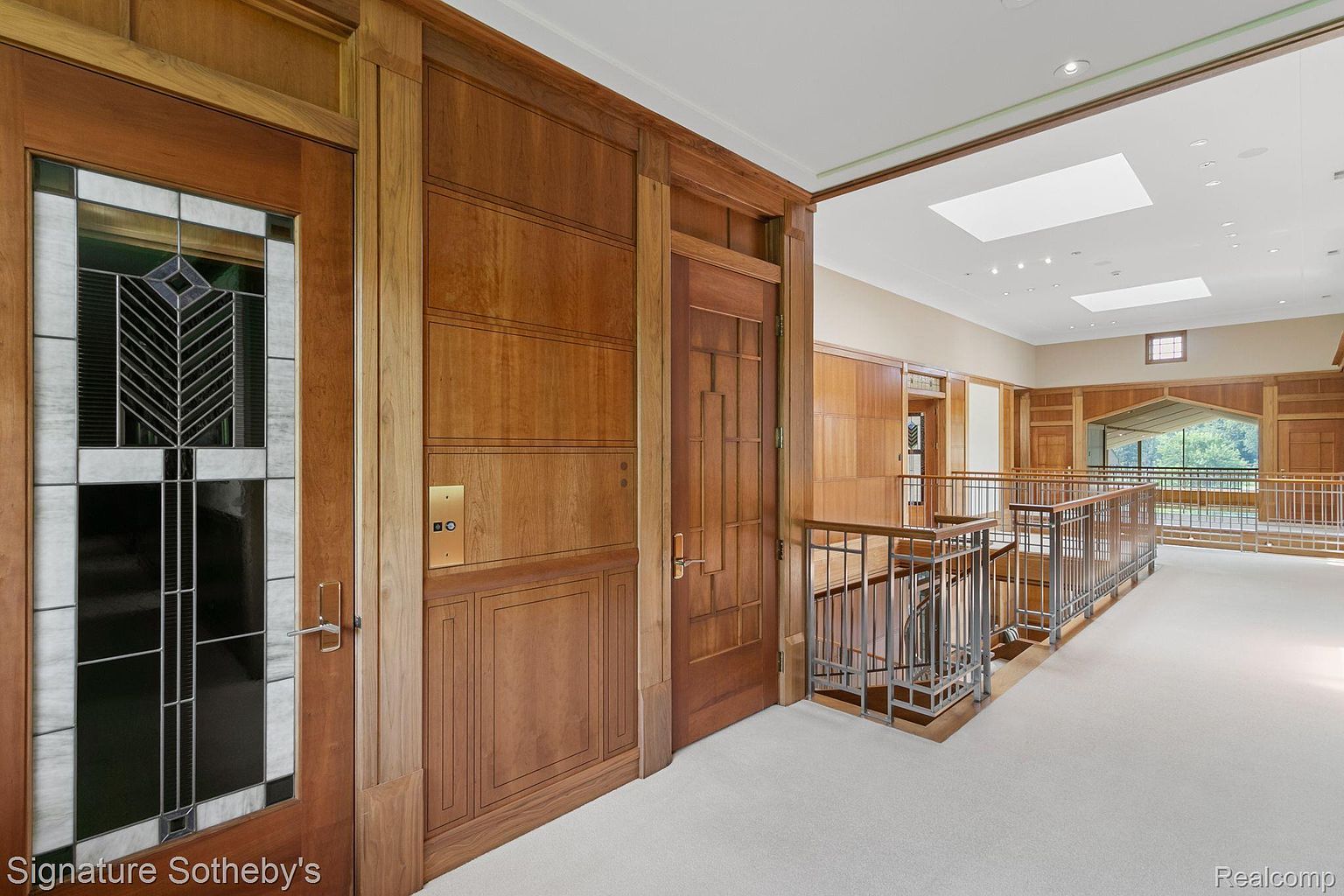 This interior shot showcases a hallway with rich wood paneling and architectural details. A stained glass door adds character, while an elevator provides modern convenience. The hallway leads to a staircase with metal railings, creating a blend of classic and contemporary design.