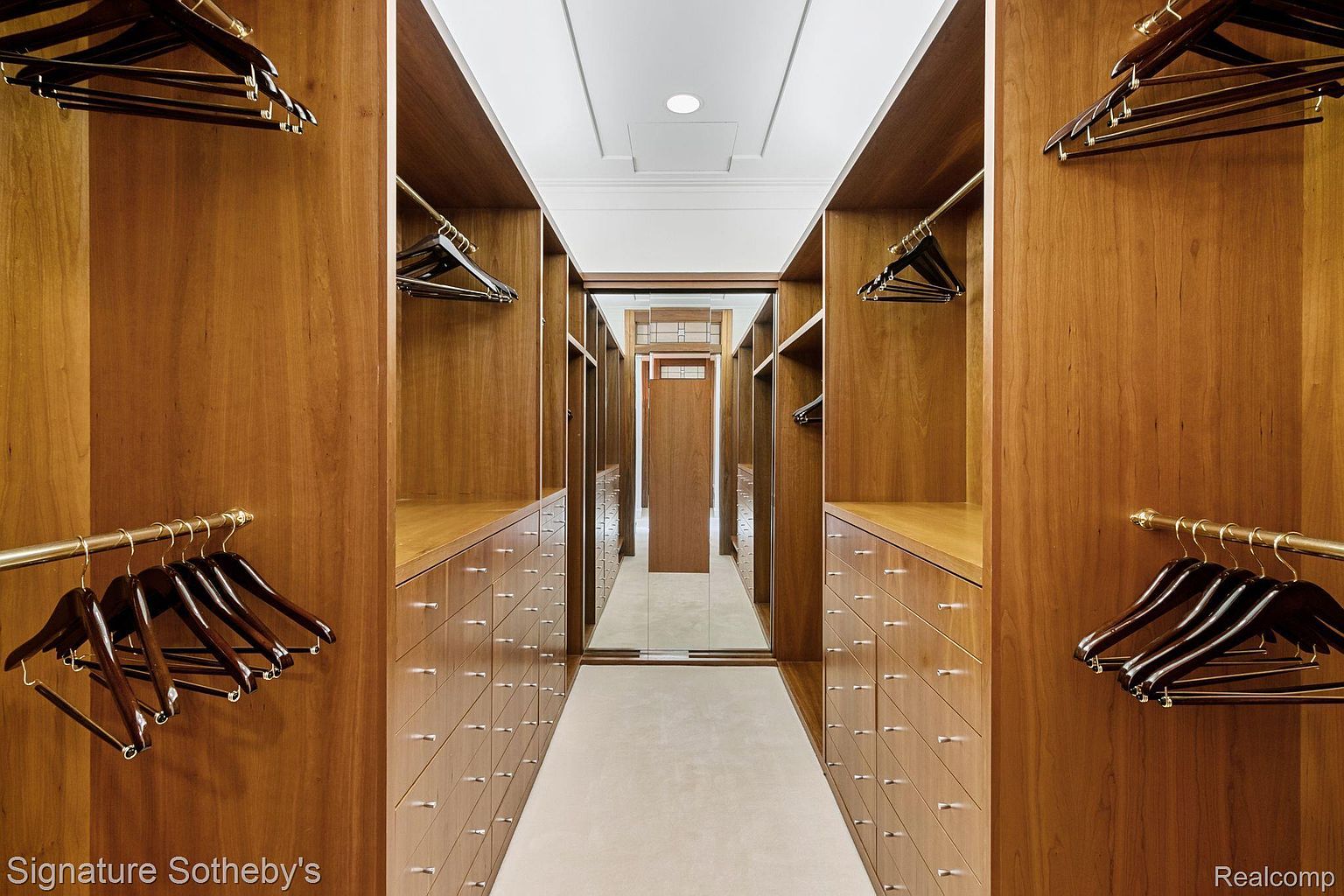 This is a well-organized walk-in closet featuring wooden cabinetry and drawers on both sides of a central walkway. The closet is equipped with hanging rods and numerous drawers, providing ample storage space. The design is elegant and functional, ideal for a luxury home.