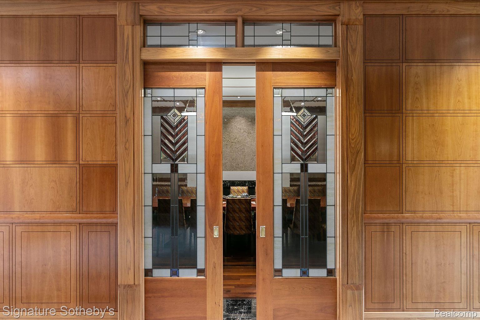 The image showcases an ornate, wood-framed doorway with stained glass panels. The door features a geometric design in the glass, adding a touch of elegance and privacy. The surrounding wood paneling complements the door, creating a cohesive and luxurious architectural detail.
