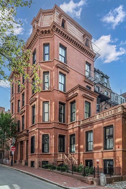 This is a stately, multi-story brick building with intricate architectural details, including bay windows, decorative cornices, and a mansard roof. The building exudes a sense of classic elegance and historical charm, enhanced by the well-maintained facade and wrought-iron fencing. The perspective is from street level, capturing the full height and grandeur of the building.