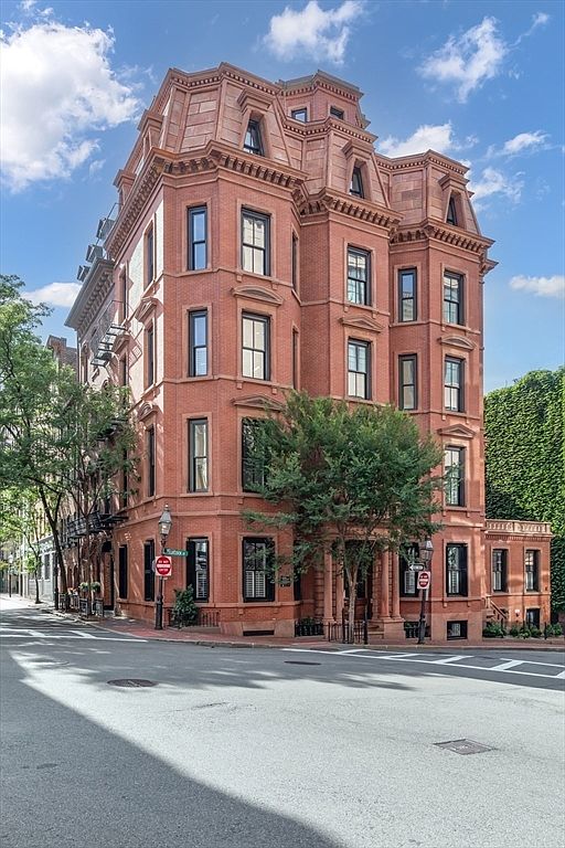 This is a stunning front view of a grand, multi-story brick building, likely a luxury apartment or a historic residence. The building features intricate architectural details, including ornate window frames, a mansard roof, and a symmetrical facade. Lush greenery surrounds the base of the building, adding to its curb appeal and creating a sense of urban elegance.