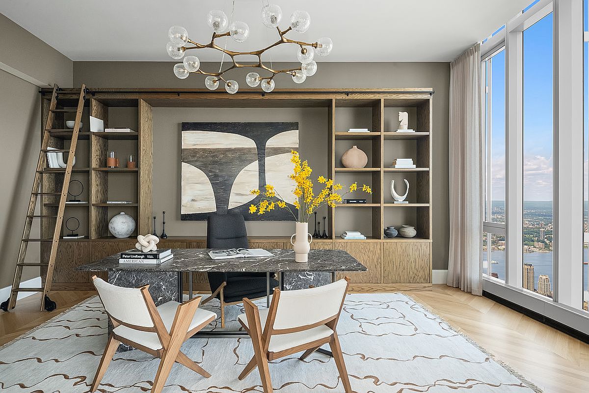 This sophisticated home office features a striking marble-topped desk, a dark ergonomic chair, and two modern wooden chairs, all set upon a patterned area rug. A large, custom-built oak bookshelf with an integrated rolling ladder spans the back wall, framing a contemporary abstract painting. The room is bathed in natural light from floor-to-ceiling windows that offer a breathtaking, high-altitude view of the city and river below.
