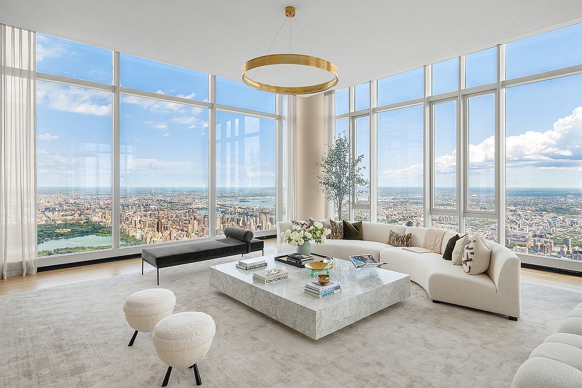 This luxurious, high-rise living room features floor-to-ceiling windows that offer a breathtaking, panoramic view of the city skyline and a large park. The space is anchored by a sophisticated, curved white sofa, a large marble coffee table, and a minimalist black daybed, all set upon a plush, neutral-toned area rug. A modern, circular gold chandelier hangs from the ceiling, adding a touch of elegance to the bright, airy, and contemporary atmosphere.