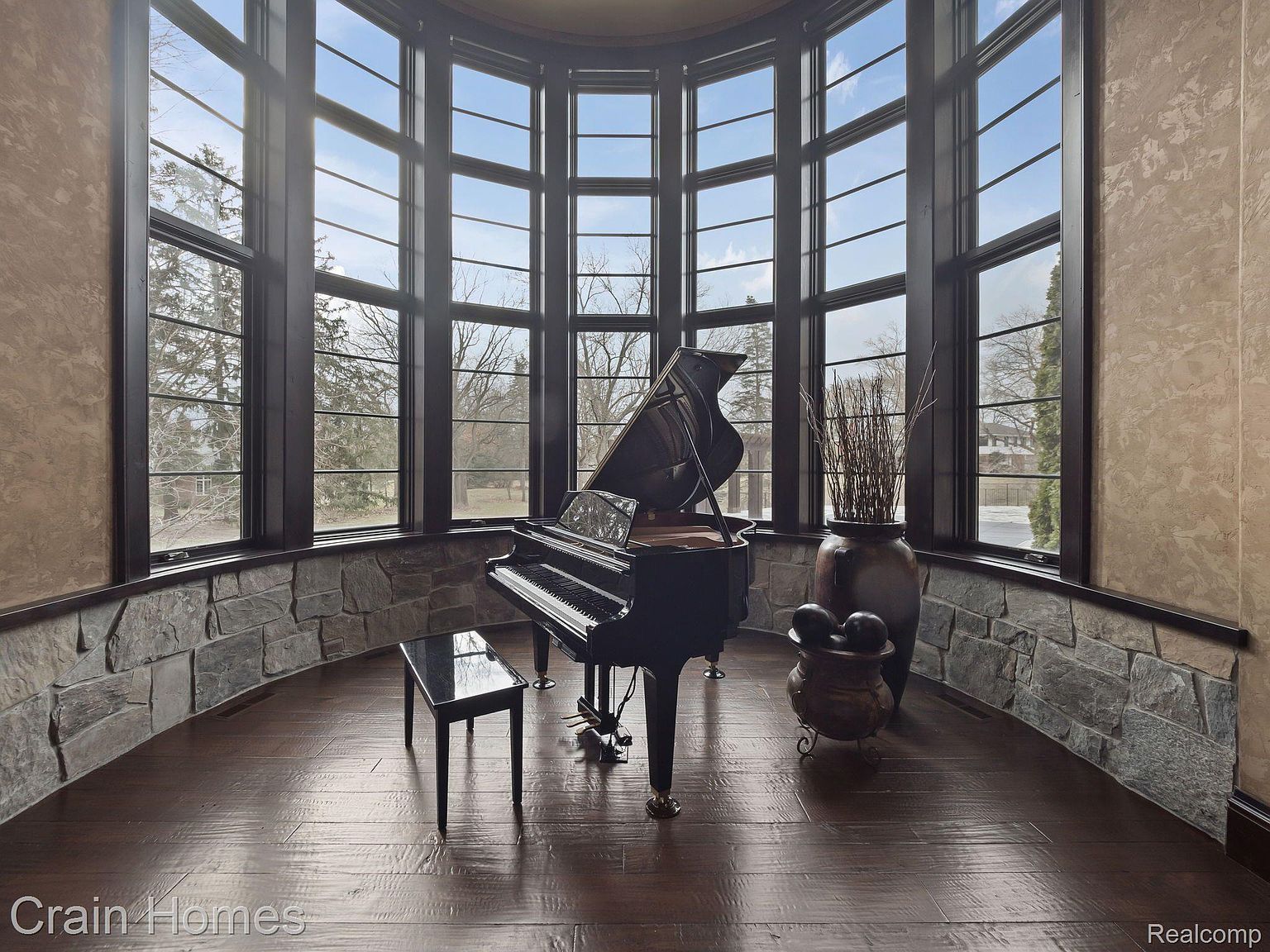 This interior shot showcases a luxurious living room featuring a grand piano as its centerpiece. The room is bathed in natural light from a large, curved window wall, complemented by stone accents and hardwood flooring. The overall impression is one of elegance and sophistication, perfect for a discerning buyer.