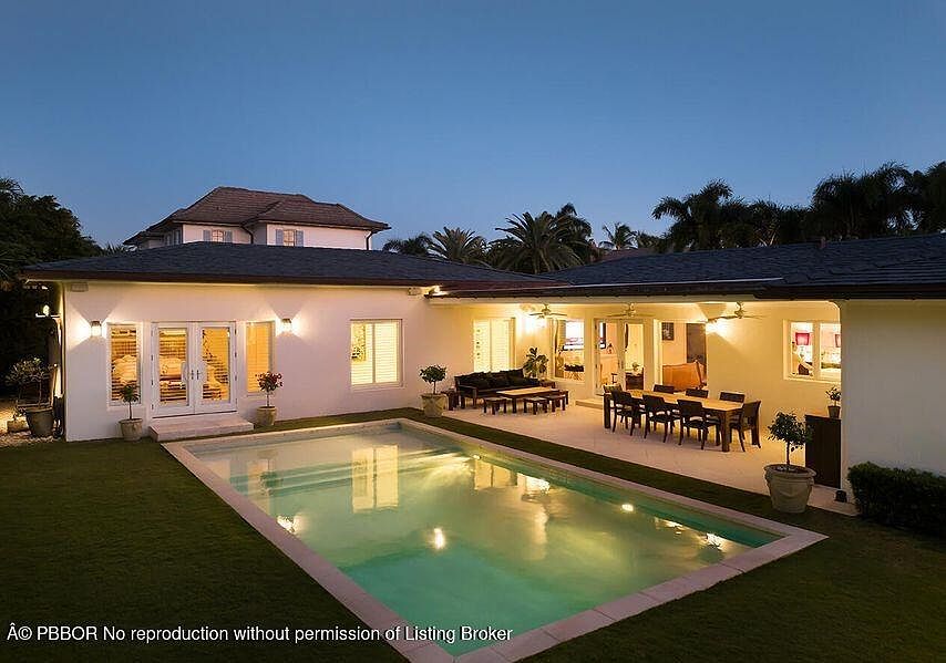 This image showcases a luxurious backyard featuring a rectangular swimming pool as the focal point. The pool is surrounded by a well-maintained lawn and a patio area with outdoor seating and dining arrangements. The architecture of the house is visible in the background, suggesting a seamless indoor-outdoor living experience.