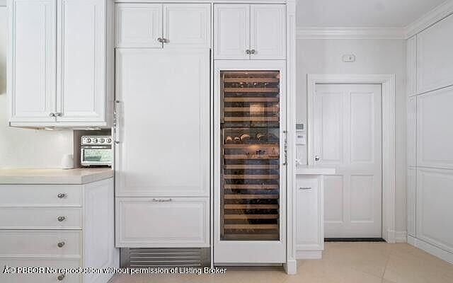 This is a well-lit kitchen featuring white cabinetry, including overhead cabinets and a built-in wine cooler. The kitchen also includes a refrigerator integrated into the cabinetry. The overall impression is clean and modern, with a focus on storage and functionality.