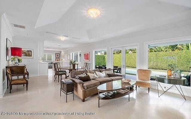 This is an interior shot of a living room featuring a large brown sofa with decorative pillows, a coffee table, and a side table. The room has large windows that provide ample natural light and a view of the outdoors. The overall style is elegant and comfortable, suitable for relaxation and entertaining.