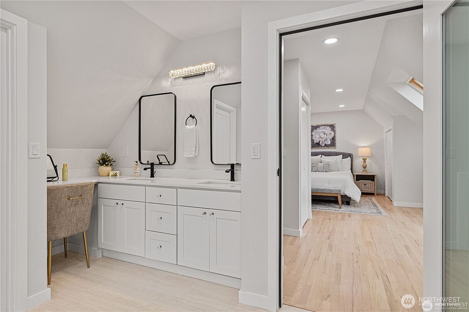 This is a bright and modern primary bathroom featuring a double vanity with white cabinets and black framed mirrors. The countertop is a light-colored solid surface, and the fixtures are black. The bathroom opens into a bedroom, creating a seamless and luxurious feel.