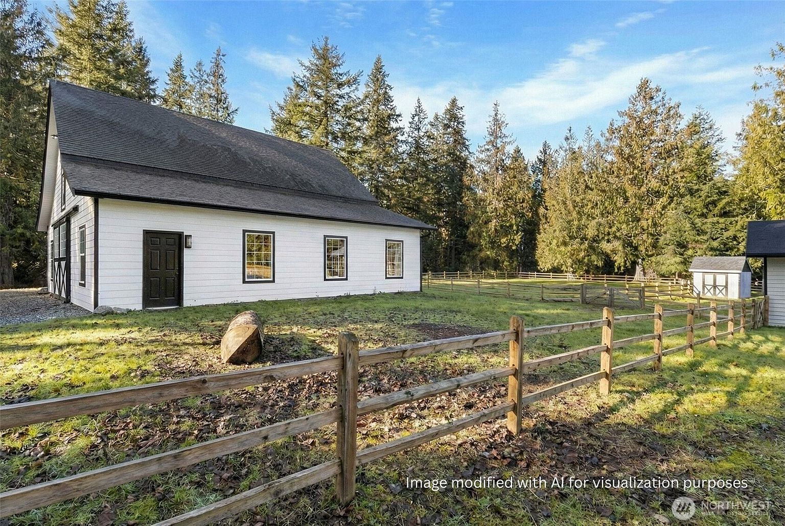The image showcases a charming exterior view of a white farmhouse-style building with a black roof and trim, complemented by a rustic wooden fence. The surrounding yard features a mix of green grass and fallen leaves, with tall evergreen trees in the background, creating a serene and inviting atmosphere. A small outbuilding is visible in the distance, adding to the property's appeal.