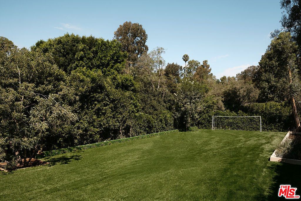 This image showcases a lush, green backyard featuring a well-maintained lawn and mature trees providing ample shade and privacy. A soccer goal is visible in the distance, suggesting recreational space. The overall impression is one of a serene and spacious outdoor area, perfect for relaxation and activities.