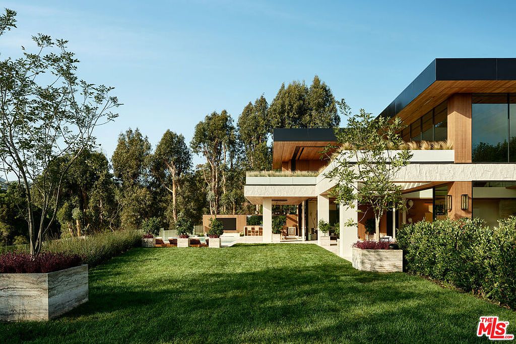 This image showcases the expansive yard and garden of a modern home. The lush green lawn is complemented by meticulously designed landscaping, including trees, shrubs, and planter boxes. The architecture of the house is visible in the background, featuring clean lines, large windows, and a seamless integration with the outdoor space, creating a serene and luxurious atmosphere.
