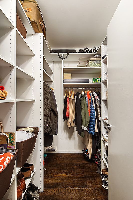 This is a well-organized walk-in closet with custom shelving and hanging rods. The closet features a variety of clothing items, shoes, and storage baskets. The dark wood flooring adds a touch of elegance, and the overall impression is one of functionality and style.