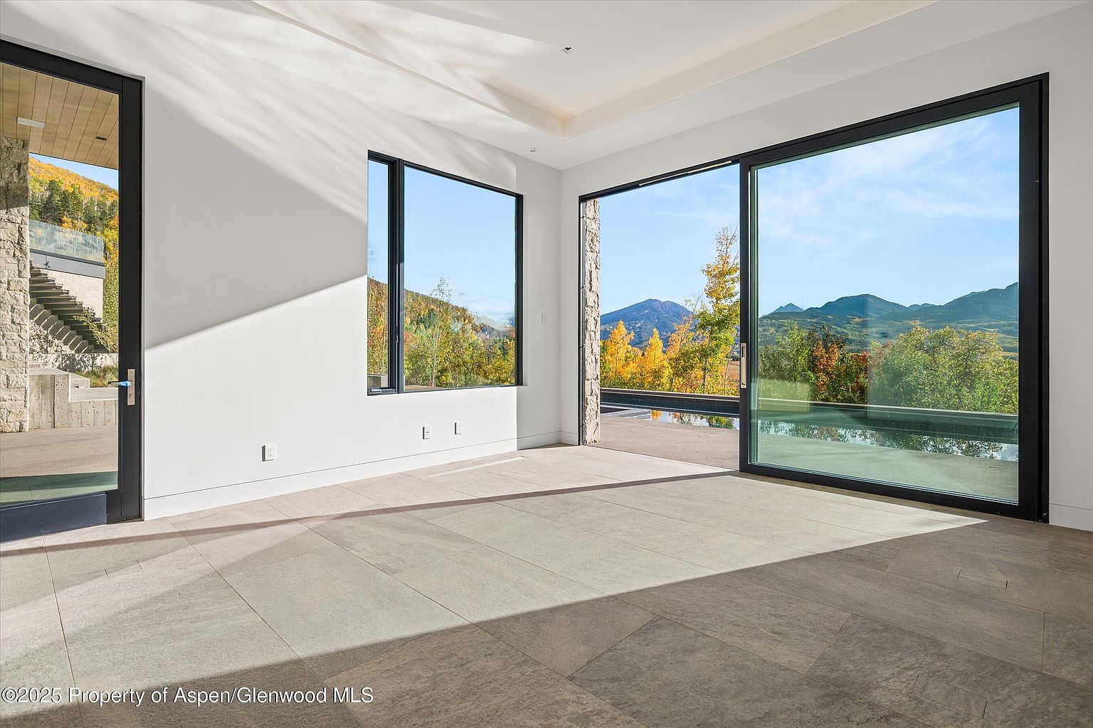 This is a bright and spacious living room with large windows offering scenic mountain views. The room features modern design elements, including sleek black window frames and light-colored tile flooring. The open layout and abundant natural light create an inviting and luxurious atmosphere, perfect for showcasing the property's connection to the surrounding landscape.