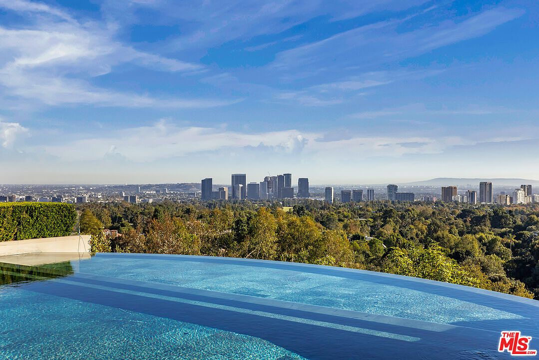 This image showcases a luxurious infinity pool overlooking a sprawling cityscape. The pool's clear blue water contrasts beautifully with the lush greenery and the distant skyline, creating a sense of serenity and exclusivity. The composition emphasizes the property's stunning views and upscale amenities.