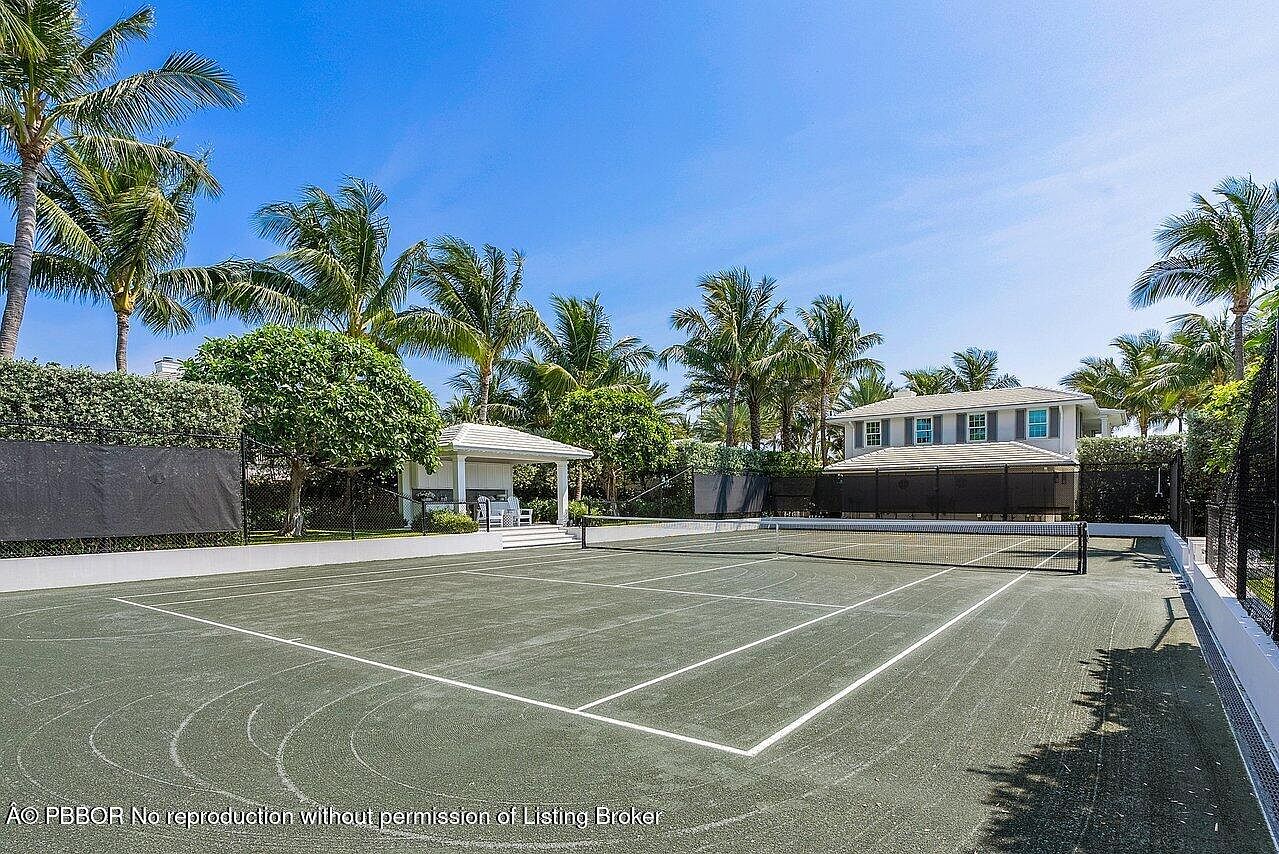 This image showcases a well-maintained tennis court surrounded by lush landscaping, including palm trees and manicured hedges. A charming gazebo sits adjacent to the court, offering a shaded seating area. The overall impression is one of luxury and leisure, highlighting the property's outdoor amenities.