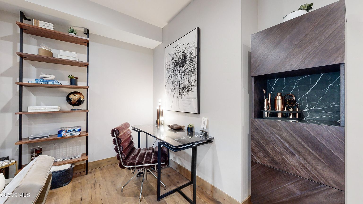 This interior shot showcases a stylish office space with a modern aesthetic. A black marble desk with a black metal frame is paired with a unique brown leather chair. A built-in bar area with dark wood and marble accents adds a touch of luxury, while a bookshelf provides storage and display space.