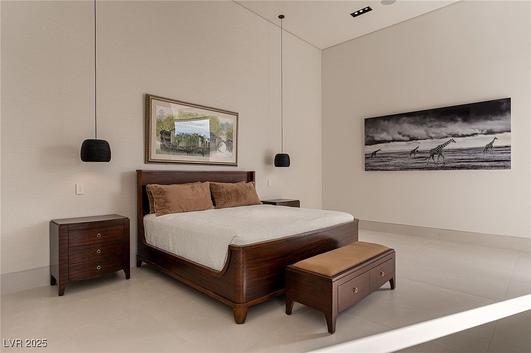 This is a primary bedroom featuring a dark wood bed frame with a light-colored quilted bedspread and brown pillows. The room is decorated with a framed landscape painting above the bed and a black and white giraffe print on the adjacent wall. Two hanging pendant lights flank the bed, and matching dark wood nightstands and a storage bench complete the sophisticated and minimalist design.