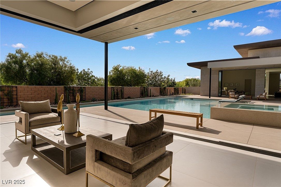 This image showcases a luxurious outdoor living space featuring a modern pool and spa area. The patio is furnished with stylish seating arrangements, including comfortable armchairs and a sleek coffee table. The pool is surrounded by a well-maintained deck, and the overall design exudes sophistication and relaxation, perfect for entertaining or unwinding.