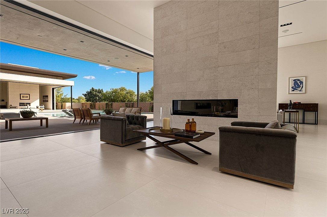 This is a spacious living room with an open floor plan that seamlessly connects to the outdoor area. The room features modern furnishings, a sleek fireplace, and large windows that offer ample natural light and views of the pool and backyard. The neutral color palette and clean lines create a sophisticated and inviting atmosphere.