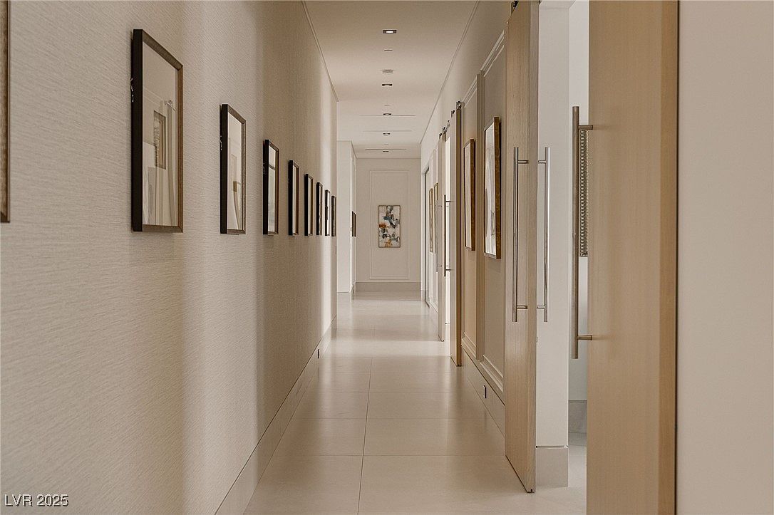 This is an interior shot of a long hallway, featuring a series of framed artwork lining the left wall. The hallway is well-lit with recessed lighting and leads to a framed opening at the end. The style is modern and minimalist, with clean lines and neutral tones, creating a sophisticated and elegant impression.
