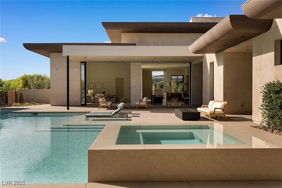 This image showcases a luxurious backyard featuring a modern home with an open-concept design that seamlessly blends indoor and outdoor living. A pristine pool and spa are the focal points, complemented by stylish patio furniture and sleek architectural details. The scene exudes sophistication and relaxation, perfect for entertaining or enjoying a private retreat.