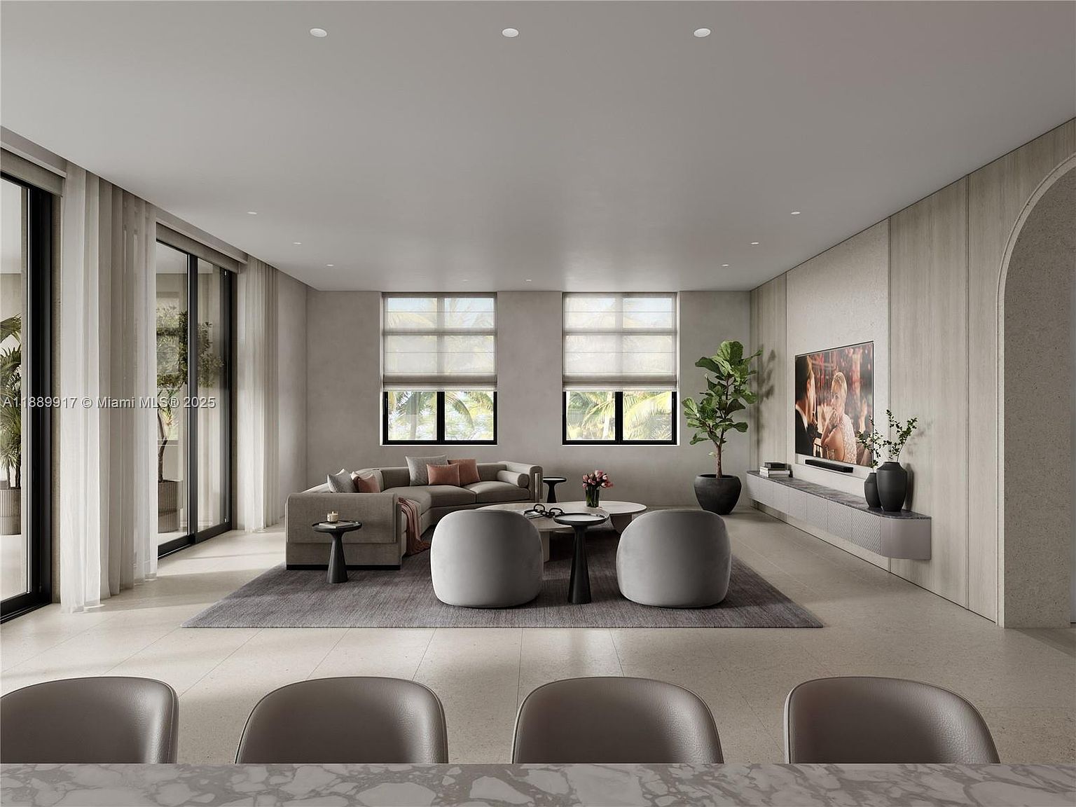 This is a spacious and modern living room featuring a neutral color palette with a large sectional sofa, two round chairs, and a sleek entertainment center with a large television. Natural light floods the room through large windows, complemented by sheer curtains. The room is styled with contemporary furniture and decor, creating a sophisticated and inviting atmosphere.