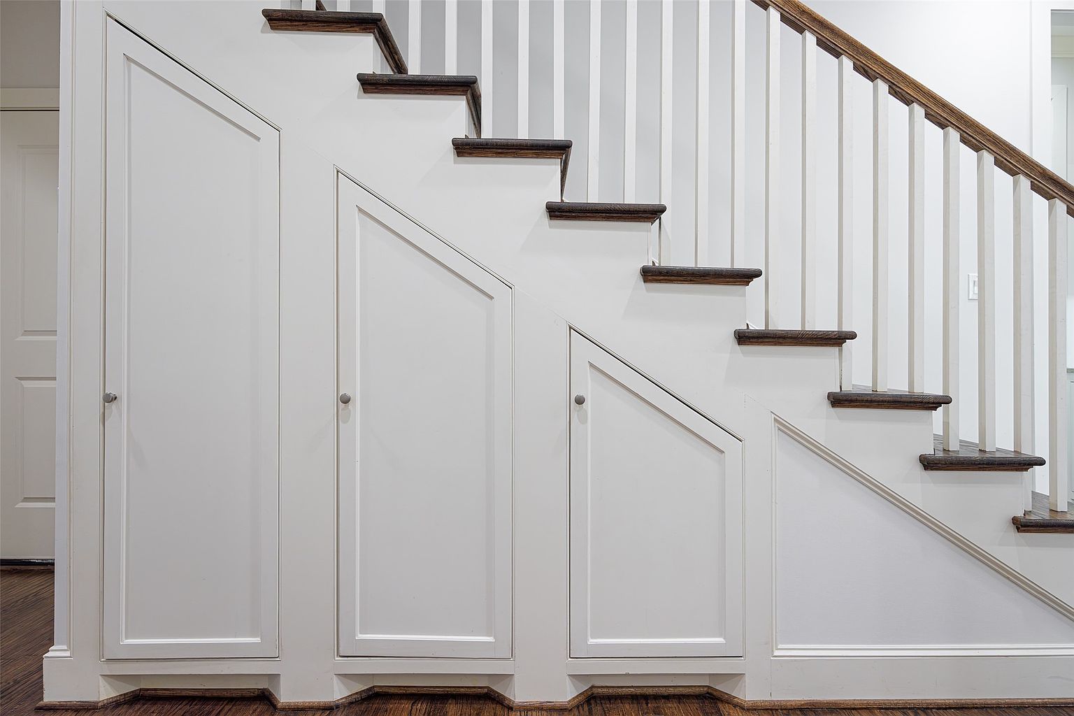 This interior shot showcases a staircase with white risers and dark wood treads, complemented by white storage cabinets built into the base of the stairs. The staircase features white balusters and a wooden handrail, adding a touch of classic elegance. The overall impression is clean, organized, and functional, highlighting the efficient use of space.