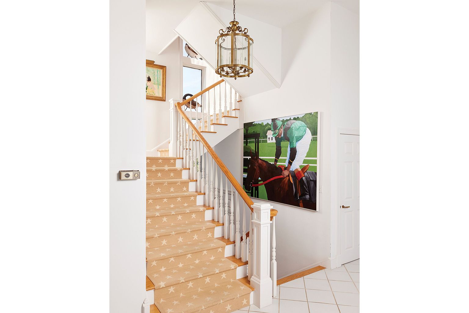 This interior shot showcases a well-lit hallway and staircase. The stairs are carpeted with a star pattern, and a wooden handrail complements the white balusters. A large painting of a jockey on a horse hangs on the wall, adding a touch of elegance, while a decorative lantern-style light fixture hangs from the ceiling, illuminating the space.