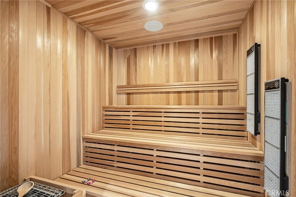 This is an interior shot of a home sauna, featuring wooden walls, ceiling, and tiered bench seating. An infrared light panel is mounted on the right wall. The sauna exudes a sense of relaxation and wellness, making it a desirable amenity for potential buyers.