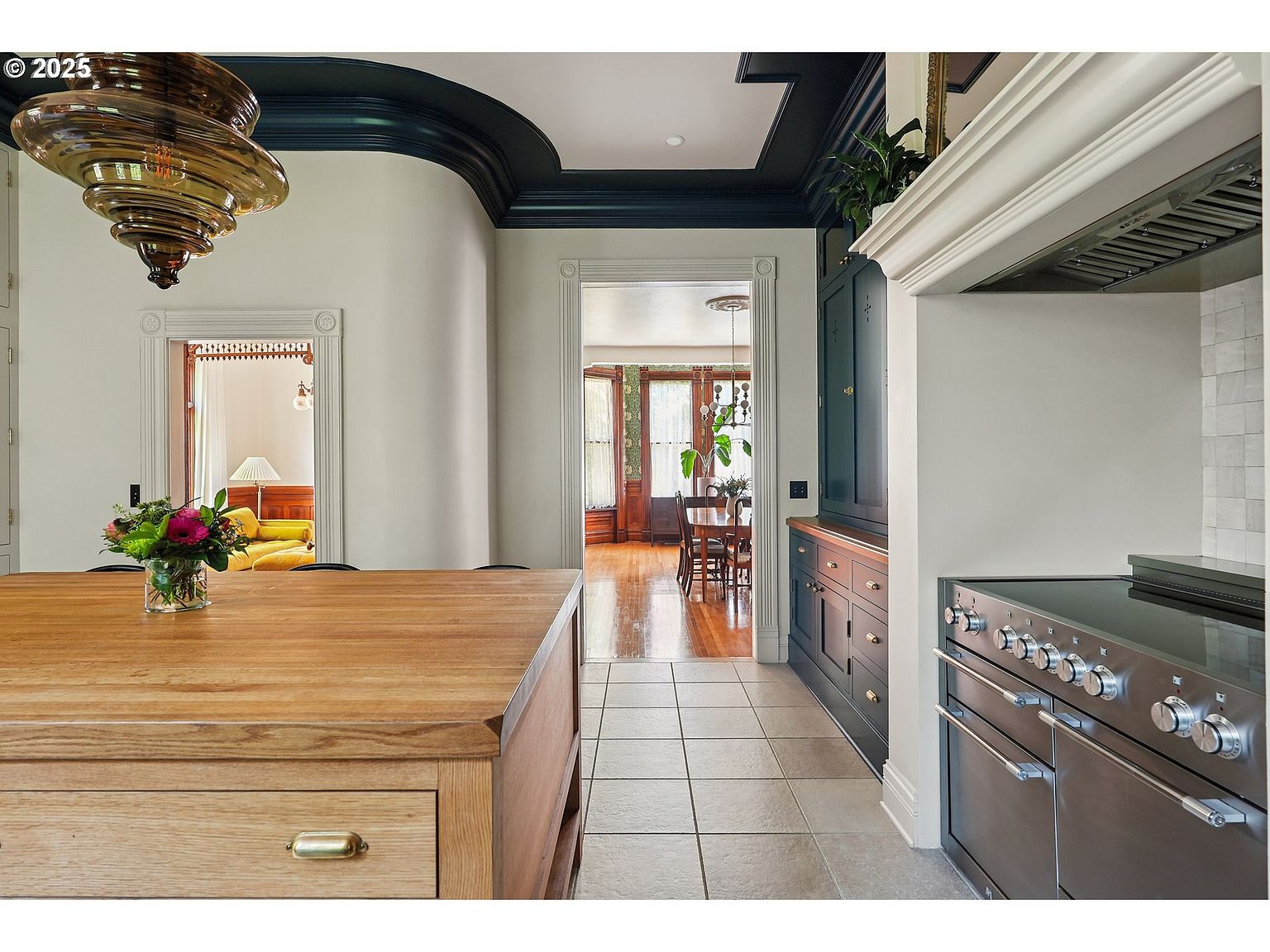 This interior shot showcases a kitchen with a blend of classic and modern elements. A wooden island takes center stage, complemented by dark cabinetry and stainless steel appliances. The space flows into a dining area, creating an open and inviting atmosphere.