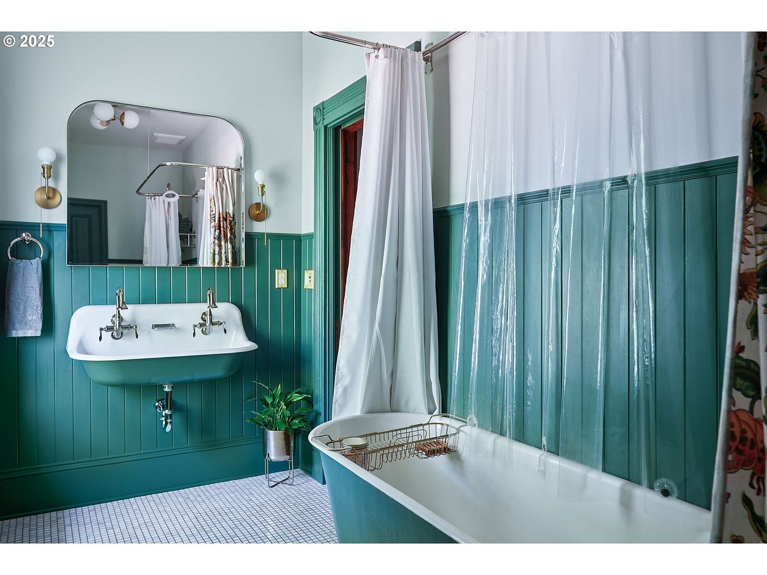 This is a charming bathroom featuring a vintage-style sink with dual faucets, set against a backdrop of teal-painted wood paneling. A clawfoot bathtub is partially visible, with a clear shower curtain and a decorative floral curtain adding a touch of elegance. The room is well-lit and has a classic, yet inviting feel, perfect for a guest bathroom.