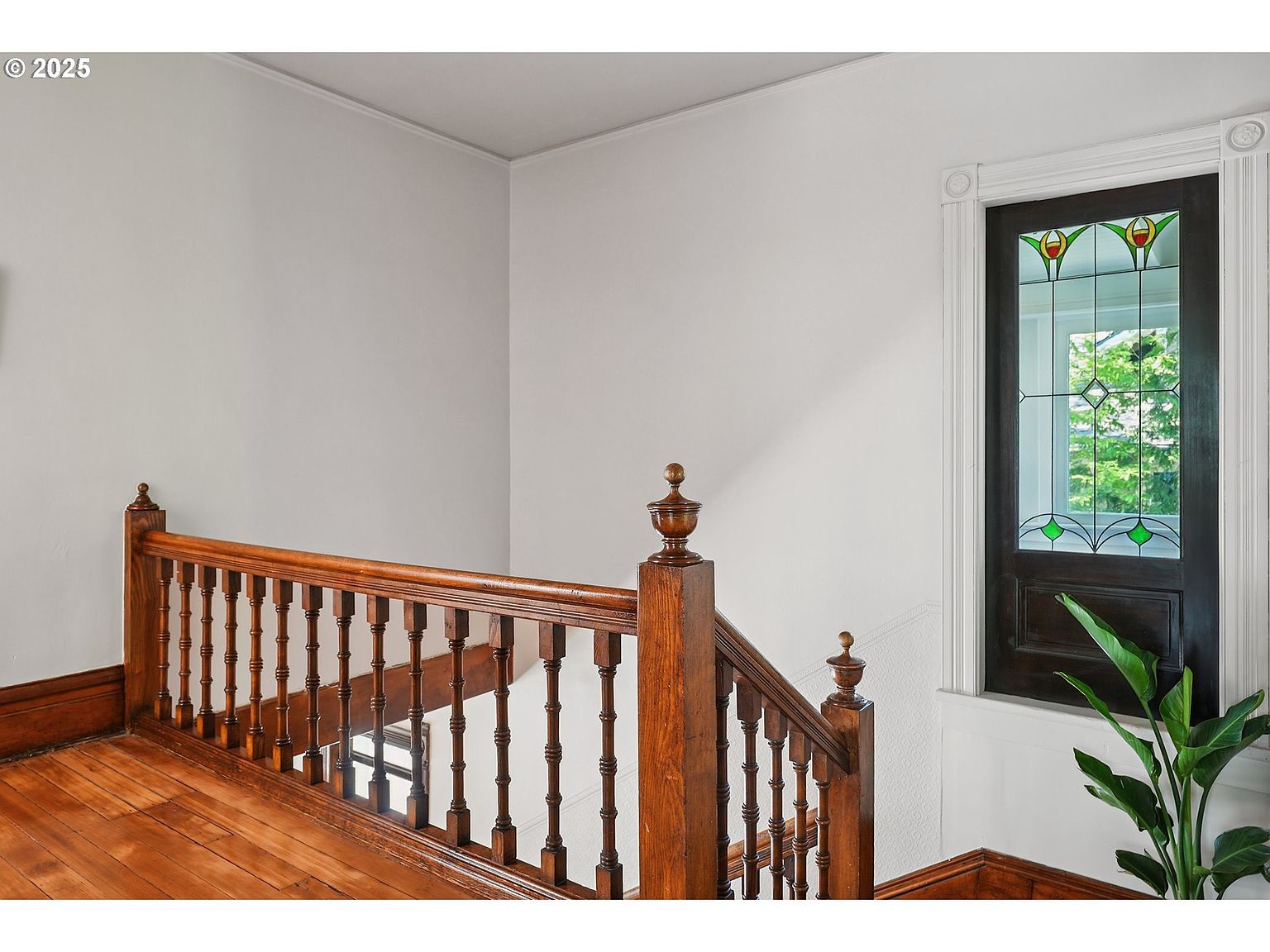 This interior shot showcases a hallway and staircase with rich, dark wood detailing. The wooden banister and spindles add a touch of classic elegance, while a stained glass window provides a unique architectural feature and natural light. The hardwood floors and neutral wall color create a warm and inviting atmosphere.