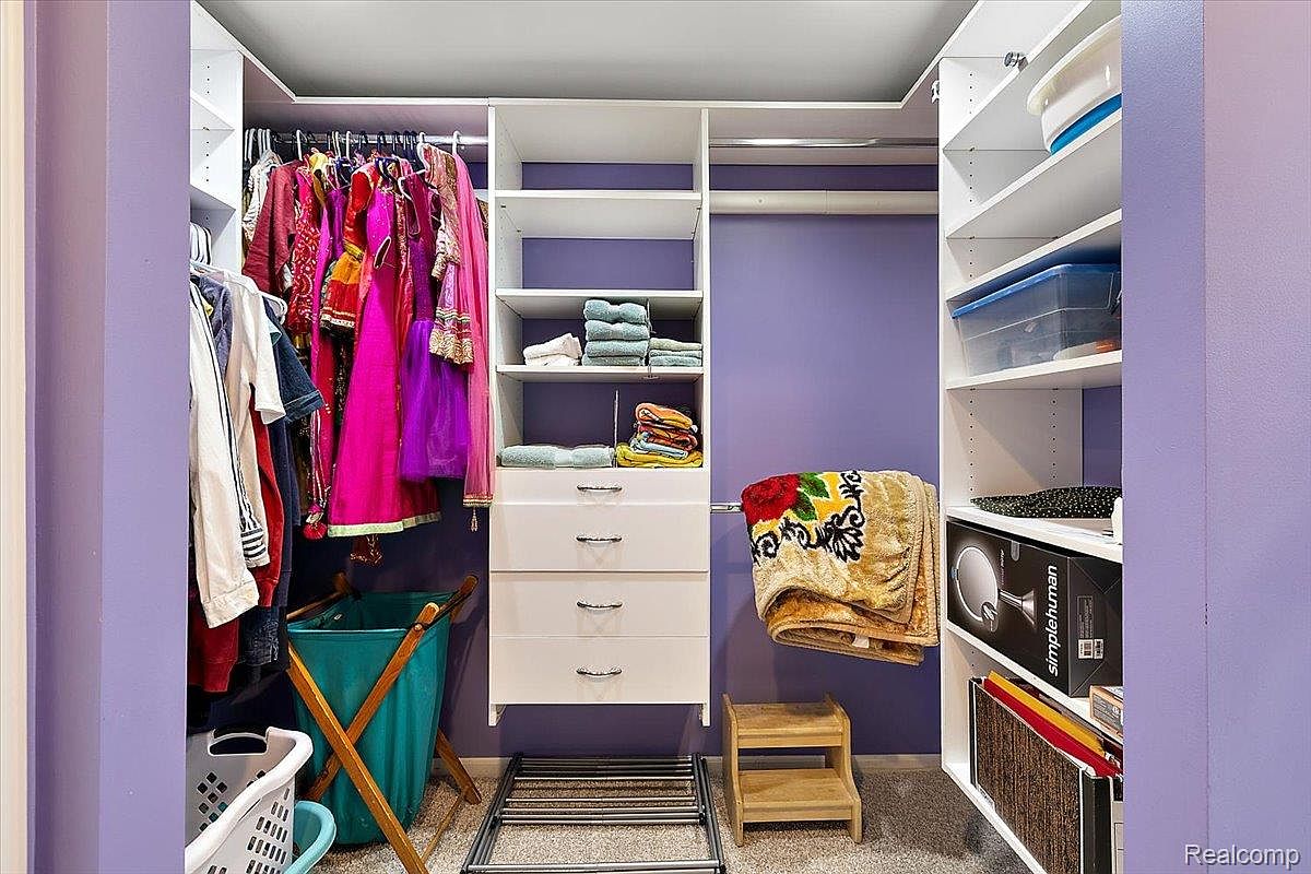 This is a well-organized walk-in closet with a purple accent wall. The closet features a combination of hanging rods, shelves, and drawers, providing ample storage space. Clothes, towels, and storage boxes are neatly arranged, showcasing the closet's functionality and design.