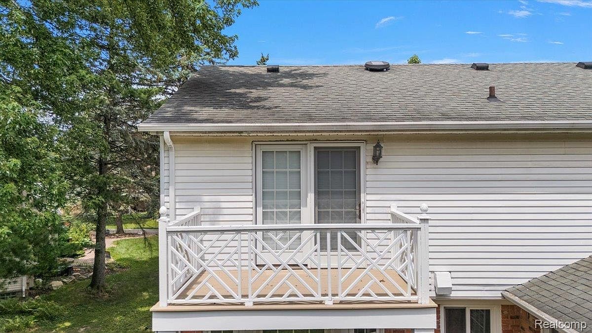 This image showcases a charming balcony with a decorative white railing and a light-colored wooden deck. The balcony is attached to a house with white siding and features a sliding glass door. The overall impression is one of a cozy and inviting outdoor space, perfect for relaxing or enjoying the view.