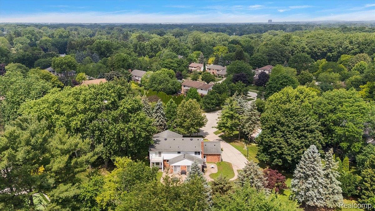 This aerial shot showcases a well-maintained house nestled among lush greenery and mature trees. The house features a brick facade, a multi-level roof, and a spacious backyard with a patio. The surrounding landscape provides privacy and a sense of tranquility, making it an appealing property.