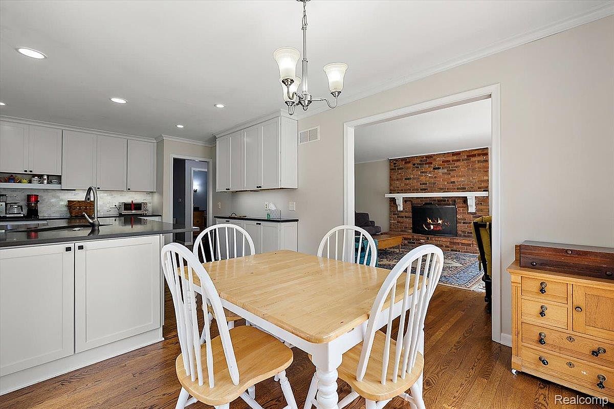 This interior shot showcases a dining area adjacent to a kitchen and living room. The dining set features a light wood table with white legs and matching chairs. The room is well-lit, and the hardwood floors add warmth to the space, creating an inviting atmosphere for family meals.