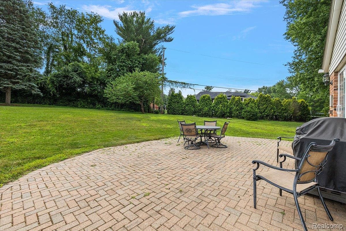 This image showcases a well-maintained backyard featuring a brick patio with outdoor seating, a lush green lawn, and mature trees providing shade and privacy. The scene evokes a sense of tranquility and outdoor living, highlighting the property's potential for relaxation and entertainment. The patio is furnished with a table and chairs, suggesting a comfortable space for dining or socializing.