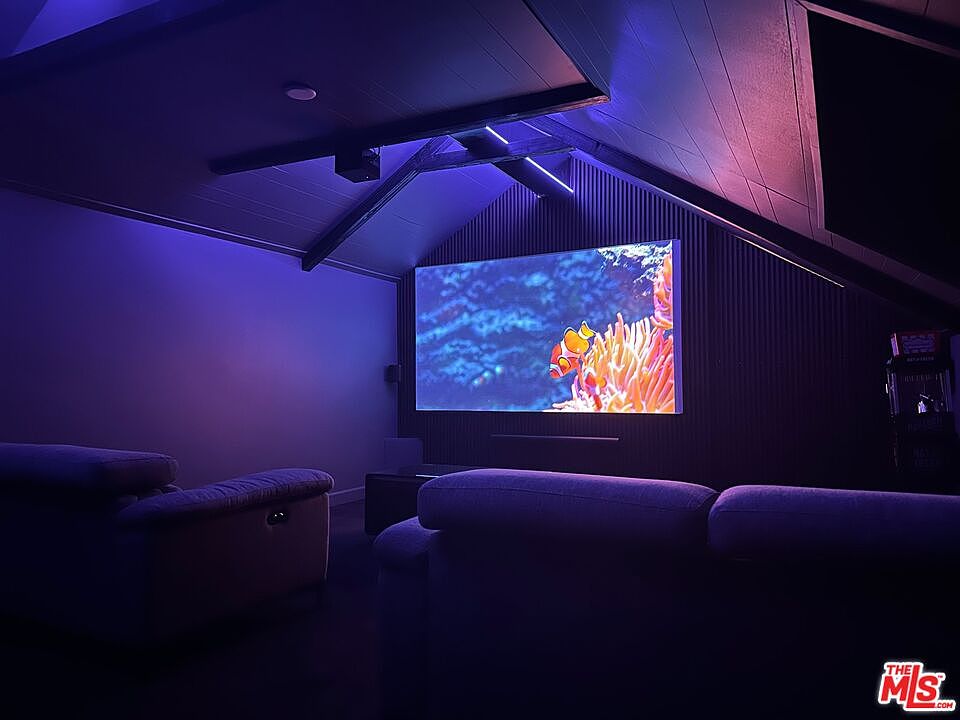 This is an interior shot of a home theater room. The room features a large screen displaying an underwater scene with clownfish, comfortable seating, and unique architectural details such as a sloped ceiling with wooden beams. The lighting is dim and atmospheric, creating a cinematic experience.