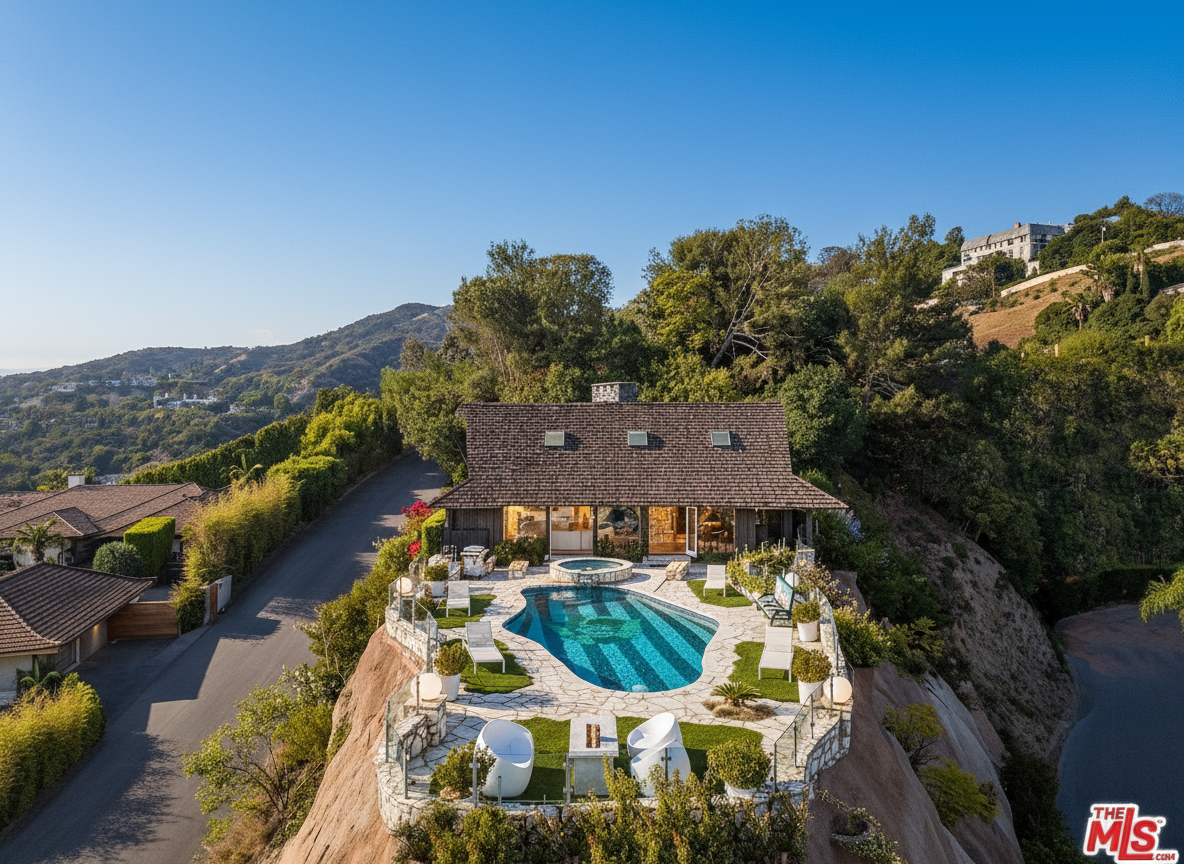 This aerial view showcases a stunning house perched on a rocky hill, complete with a unique blue-tiled pool and spa. The outdoor area is furnished with lounge chairs and seating, creating an inviting space for relaxation and entertainment. Lush greenery surrounds the property, adding to the privacy and appeal of this hilltop oasis.