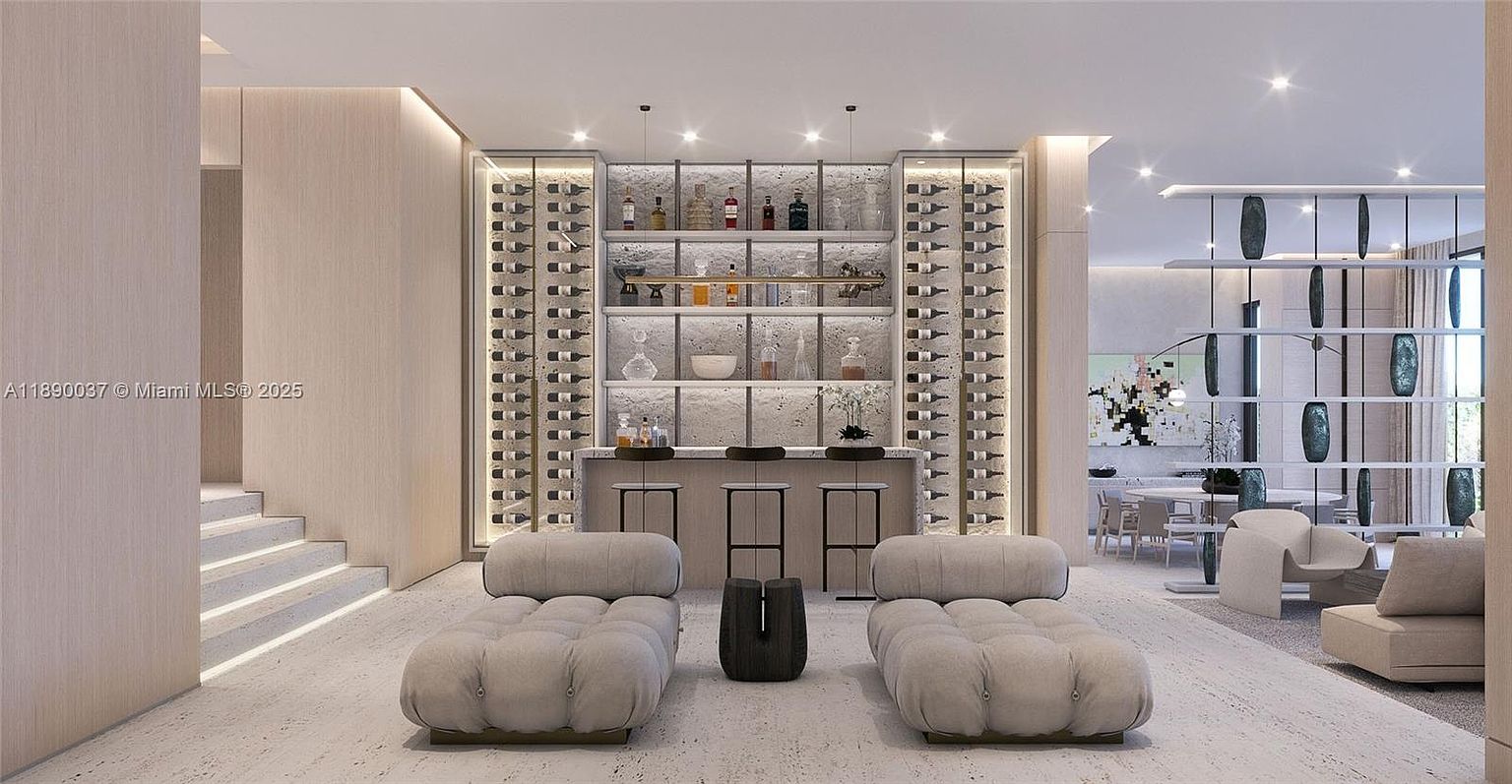 This interior shot showcases a modern living room with a built-in wine cellar and bar area. The room features neutral tones, contemporary furniture including two chaise lounges, and recessed lighting, creating a sophisticated and inviting atmosphere. The open floor plan leads to a dining area, enhancing the sense of spaciousness.