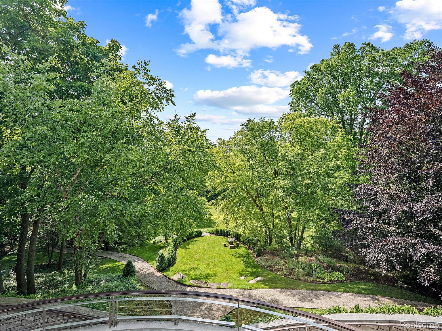 This image showcases a beautifully landscaped yard and garden. A winding stone pathway leads through lush green lawns and mature trees, creating a serene and inviting outdoor space. The view is captured from an elevated perspective, possibly a balcony or deck, offering a comprehensive view of the meticulously maintained grounds.