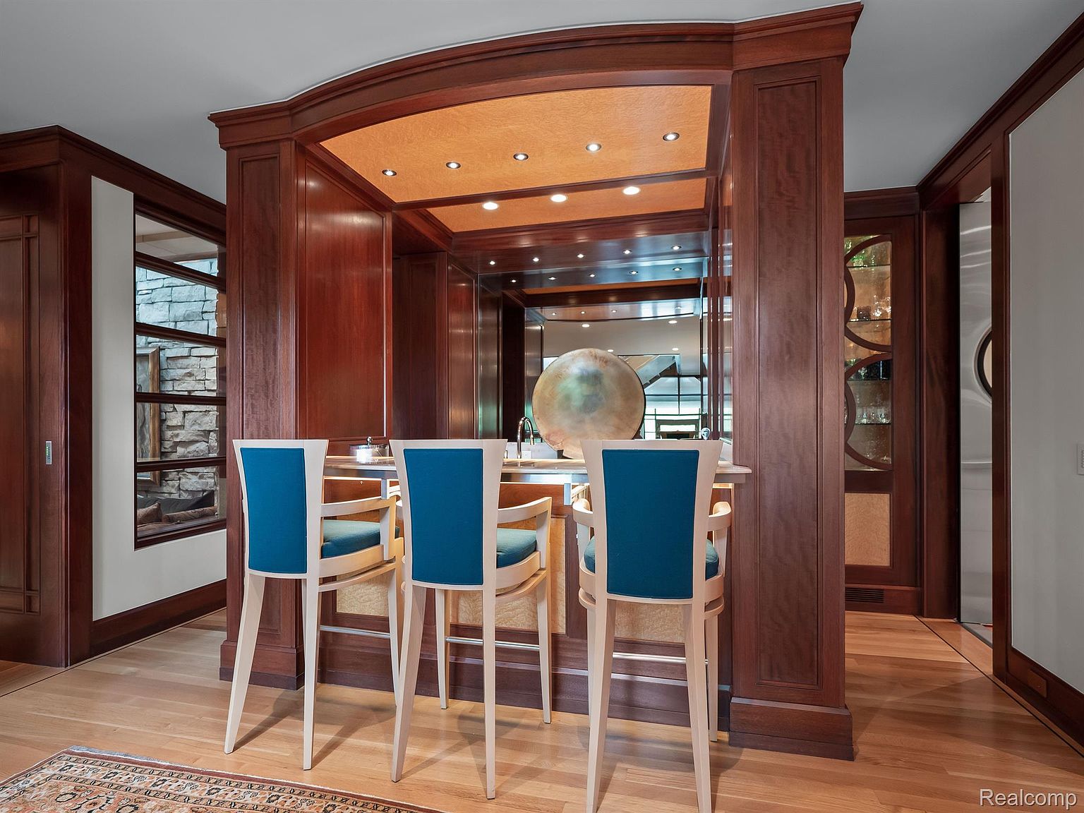 This interior shot showcases a sophisticated dining area with a built-in bar. The bar features rich wood paneling, mirrored backsplash, and stylish blue bar stools. The space is well-lit with recessed lighting, creating a warm and inviting atmosphere, perfect for entertaining.
