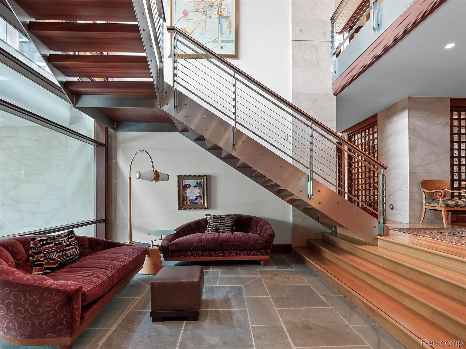 This interior shot showcases a modern hallway and staircase. The staircase features wooden steps with a metal and glass railing, complemented by a contemporary design. The space includes stylish seating arrangements and artwork, creating an elegant and inviting atmosphere.