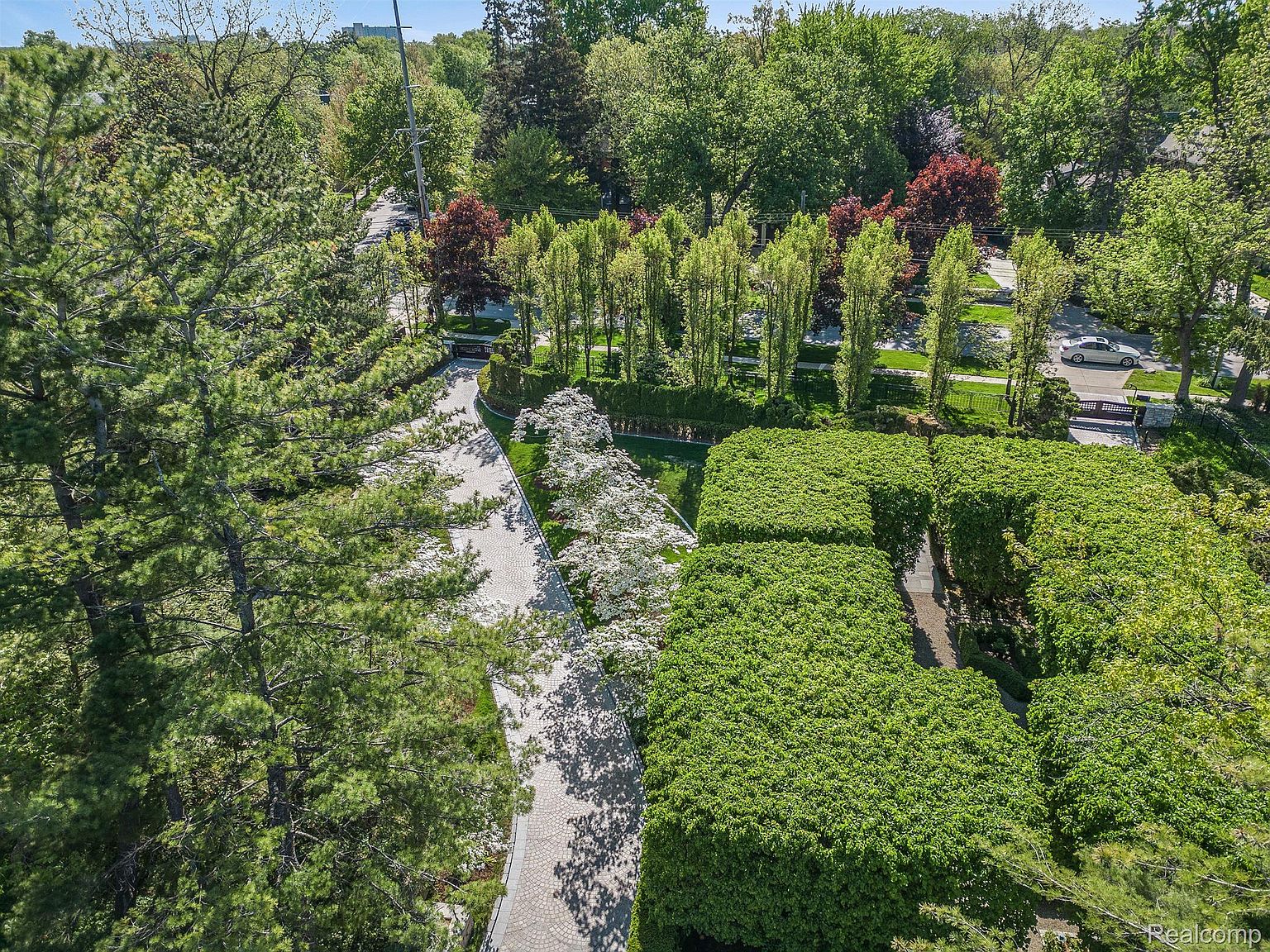 This aerial shot showcases a meticulously landscaped property with lush greenery, including manicured hedges and mature trees. A winding stone pathway leads through the garden, adding a touch of elegance. The overall impression is one of privacy and sophisticated outdoor living.