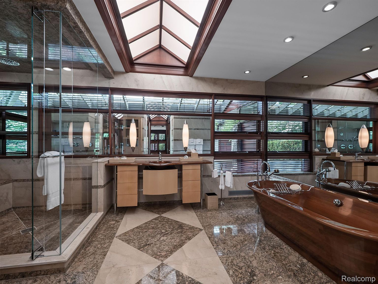 This is a luxurious primary bathroom featuring a unique wooden bathtub as a focal point, complemented by a modern vanity with a vessel sink. The room is well-lit with natural light from the skylight and windows, enhancing the elegant tile flooring and creating a spa-like atmosphere. The glass-enclosed shower adds to the contemporary design.
