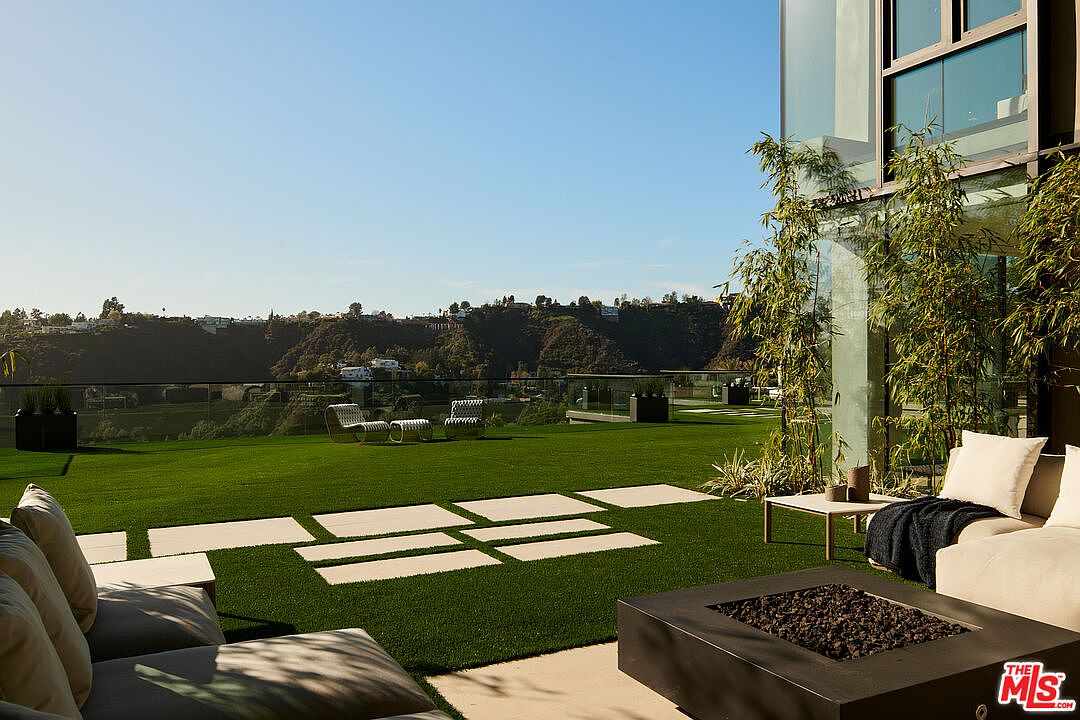 This exterior shot showcases a meticulously maintained yard featuring lush green grass and modern landscaping. A sleek fire pit and comfortable outdoor seating create an inviting space for relaxation and entertainment. The view extends to a scenic hillside, enhancing the property's appeal.