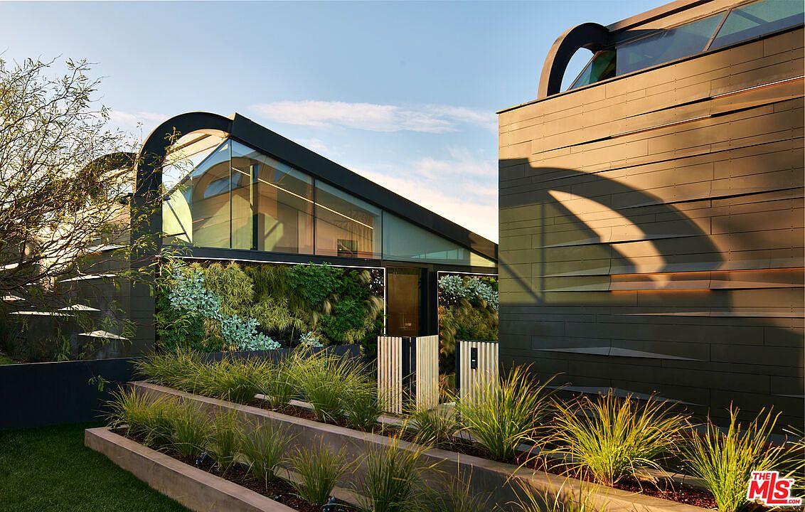 This image showcases the front exterior of a modern architectural home, featuring a unique design with curved elements, extensive glass windows, and a vertical garden. The building's facade incorporates sleek, dark materials, complemented by meticulously landscaped greenery in the foreground. The overall impression is one of sophisticated design and seamless integration with nature.