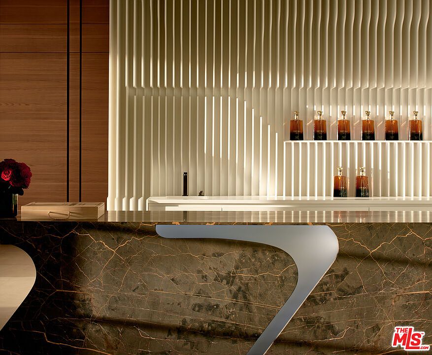 This interior shot showcases a modern hallway or reception area with a striking design. A dark, veined countertop with a unique curved edge dominates the foreground, while a textured, vertically-lined wall with built-in shelving and decorative bottles creates a visually appealing backdrop. The space exudes a sophisticated and contemporary ambiance.