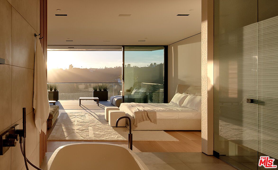 This is a luxurious primary bedroom with an open floor plan that seamlessly integrates with the bathroom and outdoor balcony. The room features a large bed, modern furniture, and floor-to-ceiling windows offering stunning views. The design emphasizes natural light and a minimalist aesthetic, creating a serene and upscale living space.